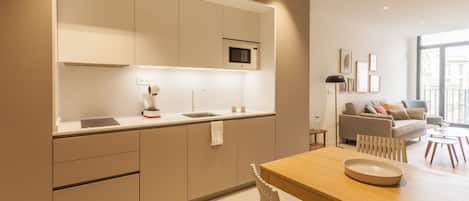 Een moderne keuken met ingebouwde apparatuur, een eethoek met een houten tafel en stoelen, en een woonkamer met een bank en salontafel.