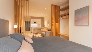 A modern hotel room with a large bed, a desk, and a kitchenette in the background. - Apartamentos Málaga Premium - Calle Granada (Málaga)