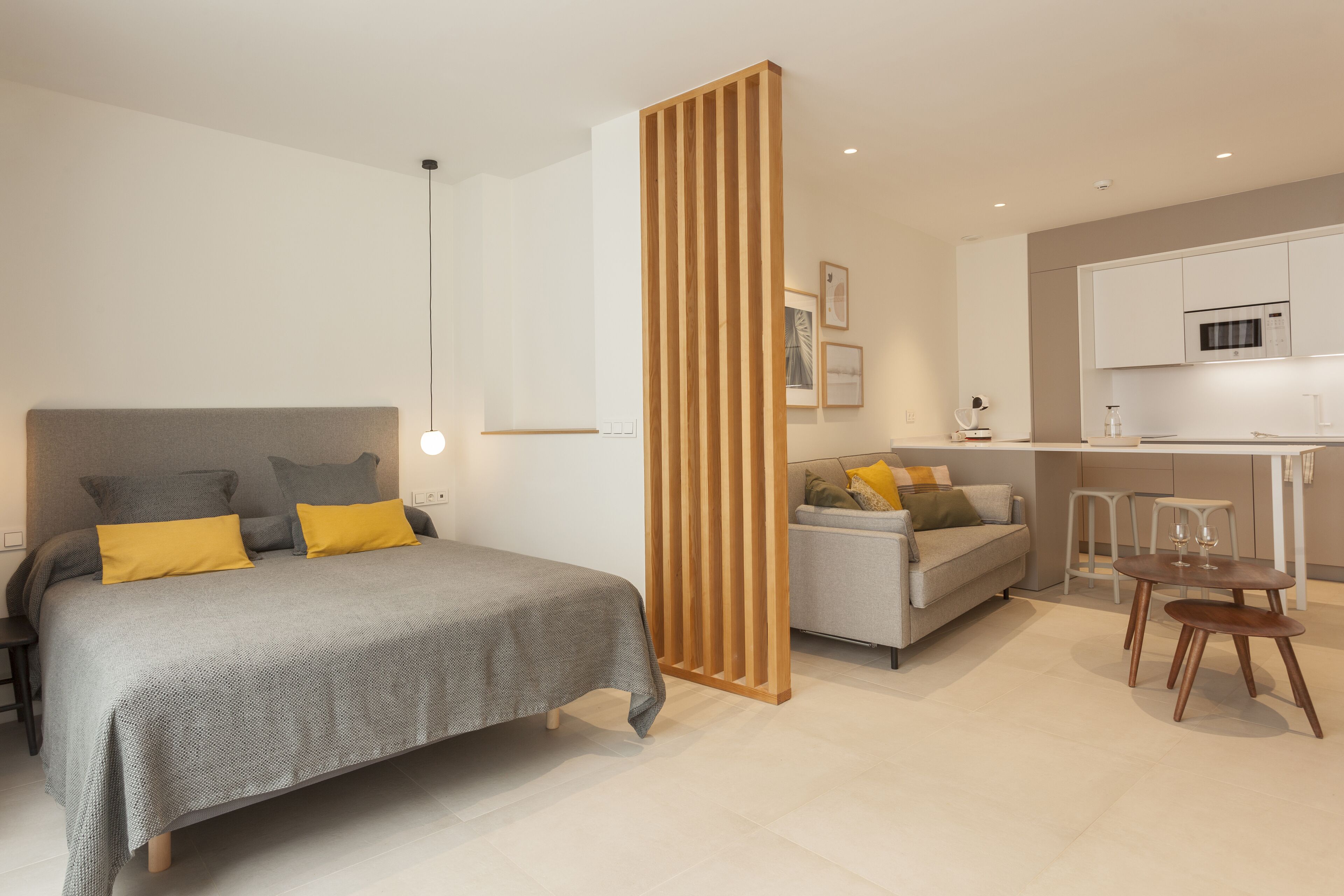 A modern bedroom with a bed, bedside tables, a wooden partition, a sofa, and a dining area with chairs.