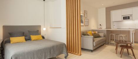 A modern bedroom with a bed, bedside tables, a wooden partition, a sofa, and a dining area with chairs.