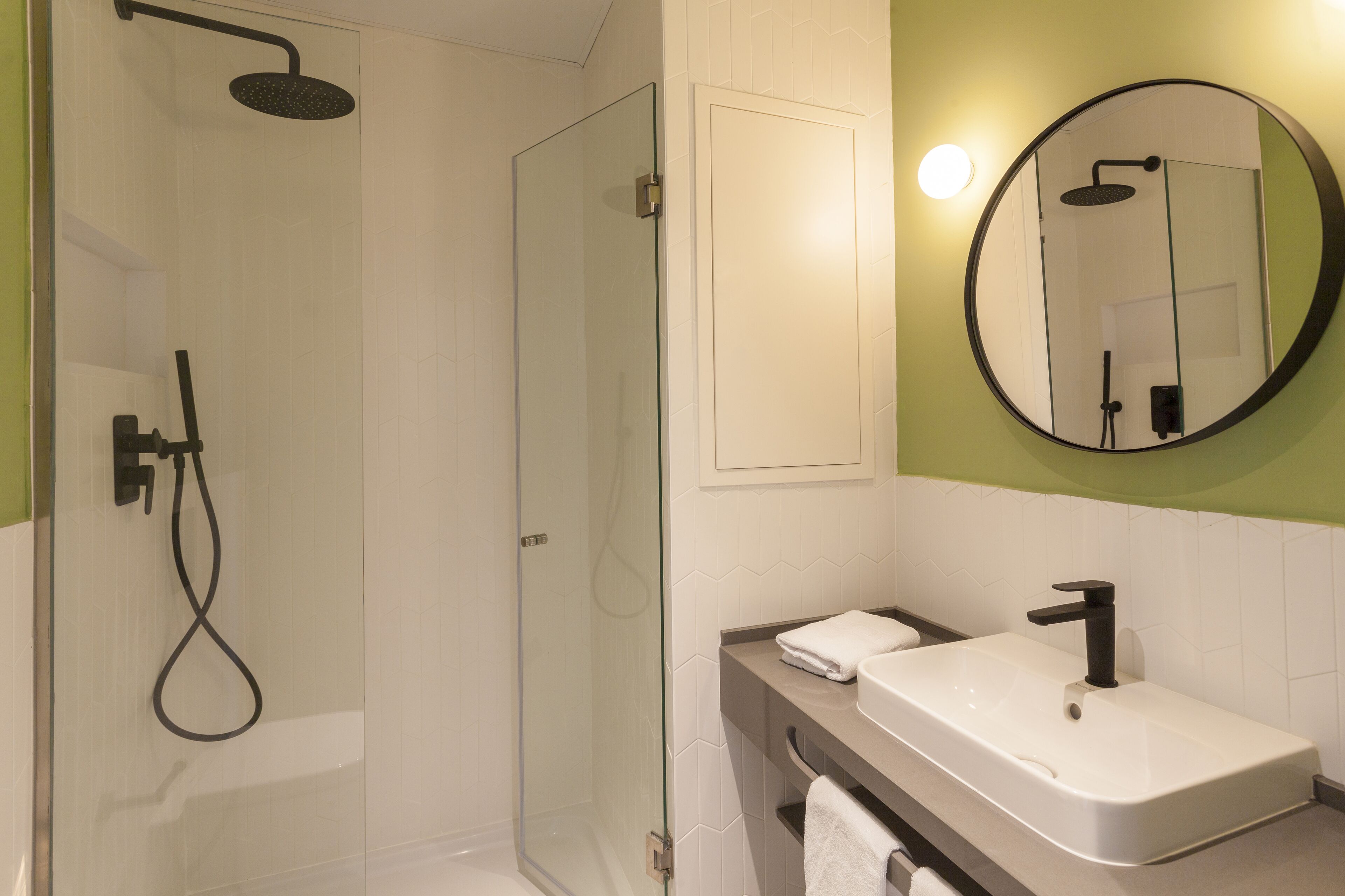 A modern bathroom with a glass-enclosed shower, a white sink with a black faucet, and a round mirror on the wall.