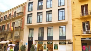 A multi-story building with a ground-level entrance, a visible storefront with signage, and a tiled pavement. - Apartamentos Málaga Premium - Calle Granada (Málaga)