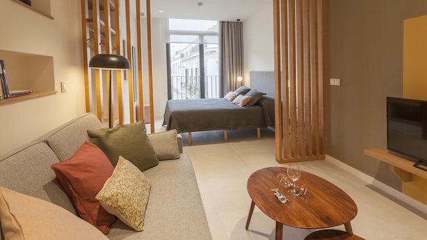 A modern hotel room with a sofa, a bed, a TV, and a balcony with a view of the city. - Apartamentos Málaga Premium - Calle Granada (Málaga)