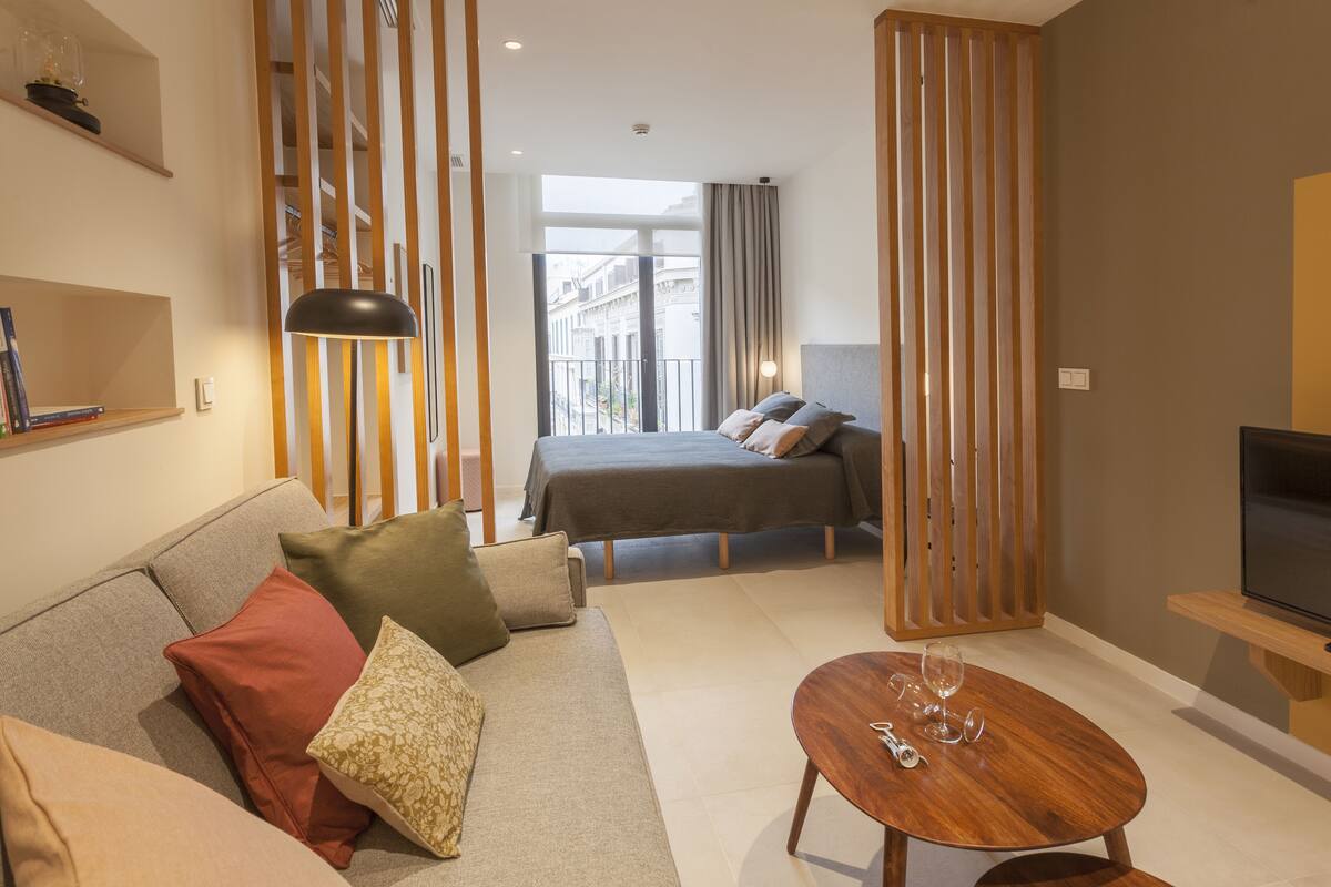 Een moderne hotelkamer met een bank, een bed, een televisie en een balkon met uitzicht over de stad.