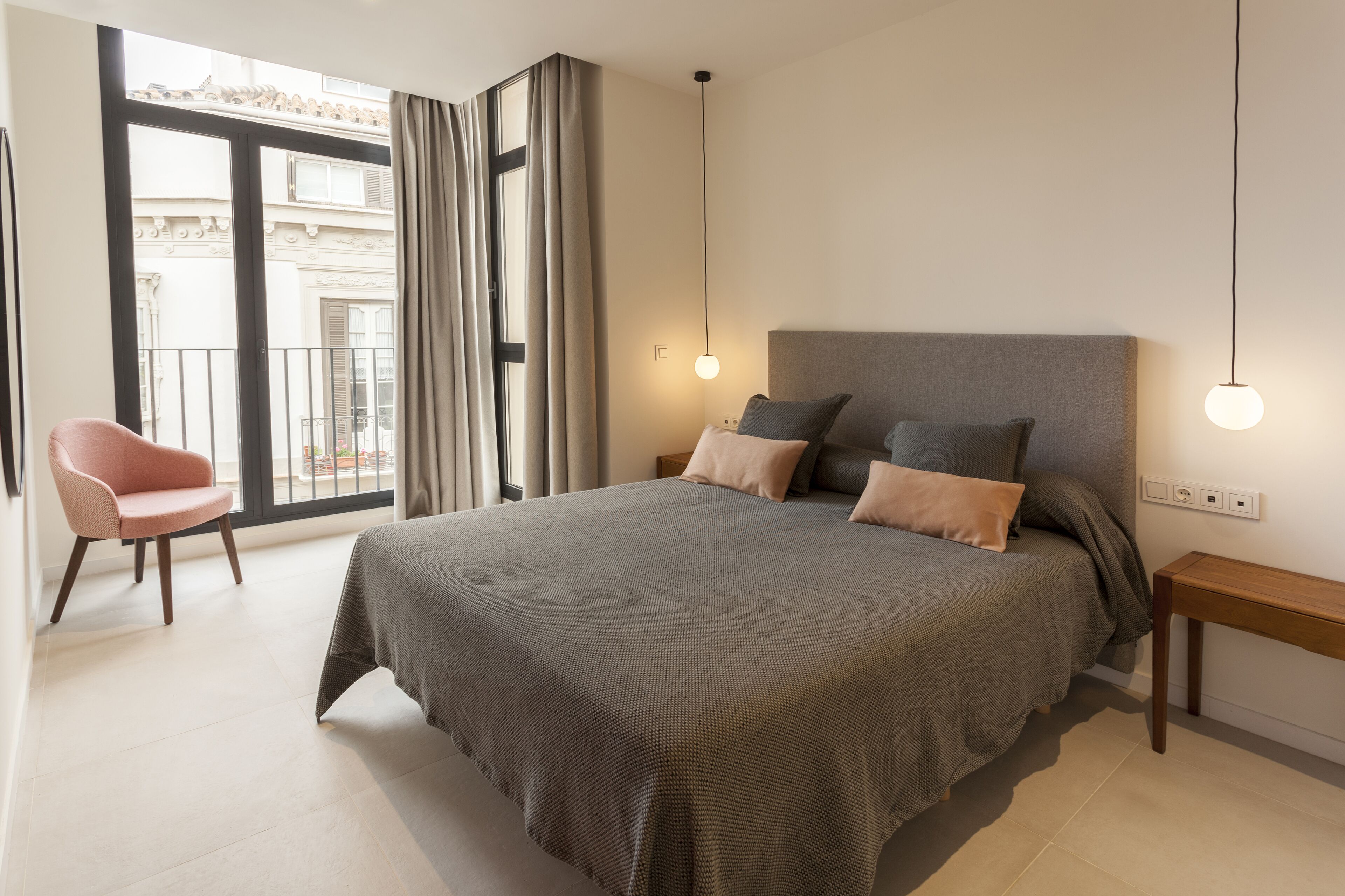Un dormitorio con una cama grande, una silla, una mesita de noche y vistas al exterior.