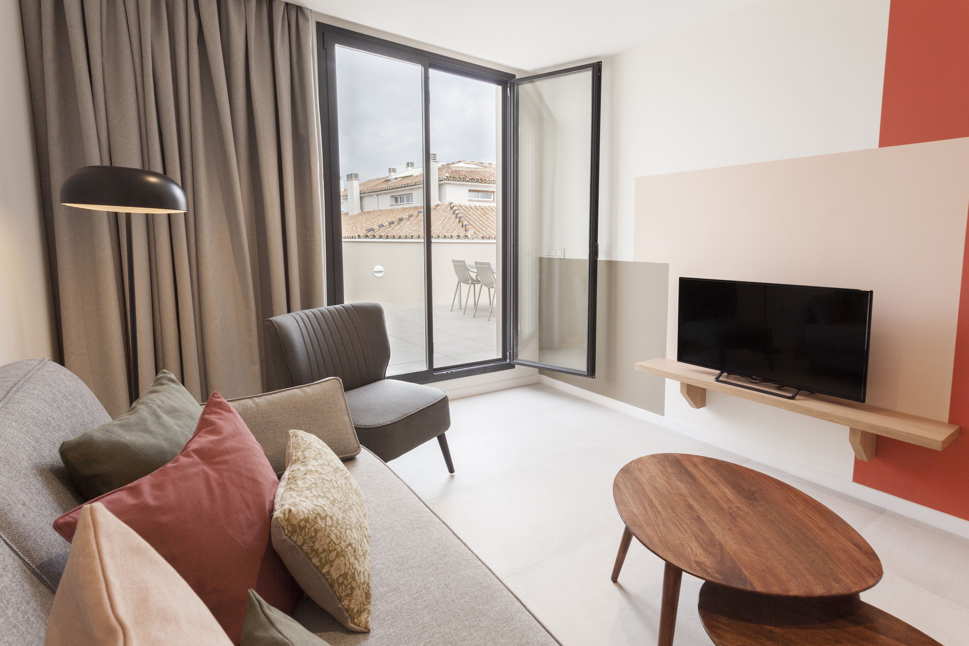 Un saló modern amb un sofà, una cadira, un televisor i una finestra gran amb cortines.