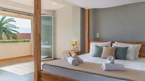 Une chambre d’hôtel moderne avec un grand lit, une tête de lit en bois et un balcon agrémenté d’un palmier.