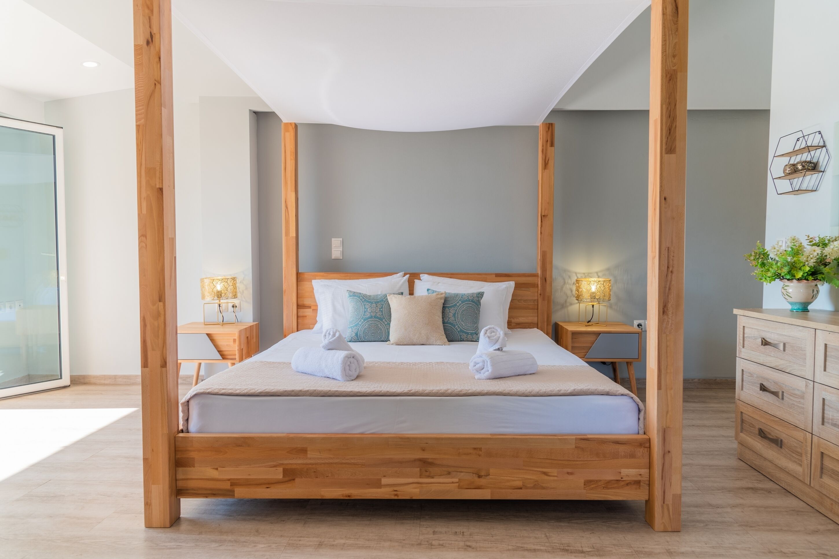 Una cama con dosel de madera, ropa de cama blanca, almohadas decorativas, dos mesitas de noche con lámparas y un aparador de madera.