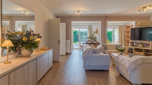Un salon spacieux, comprenant un ensemble de canapés, un téléviseur et une grande fenêtre offrant une vue sur l’extérieur.