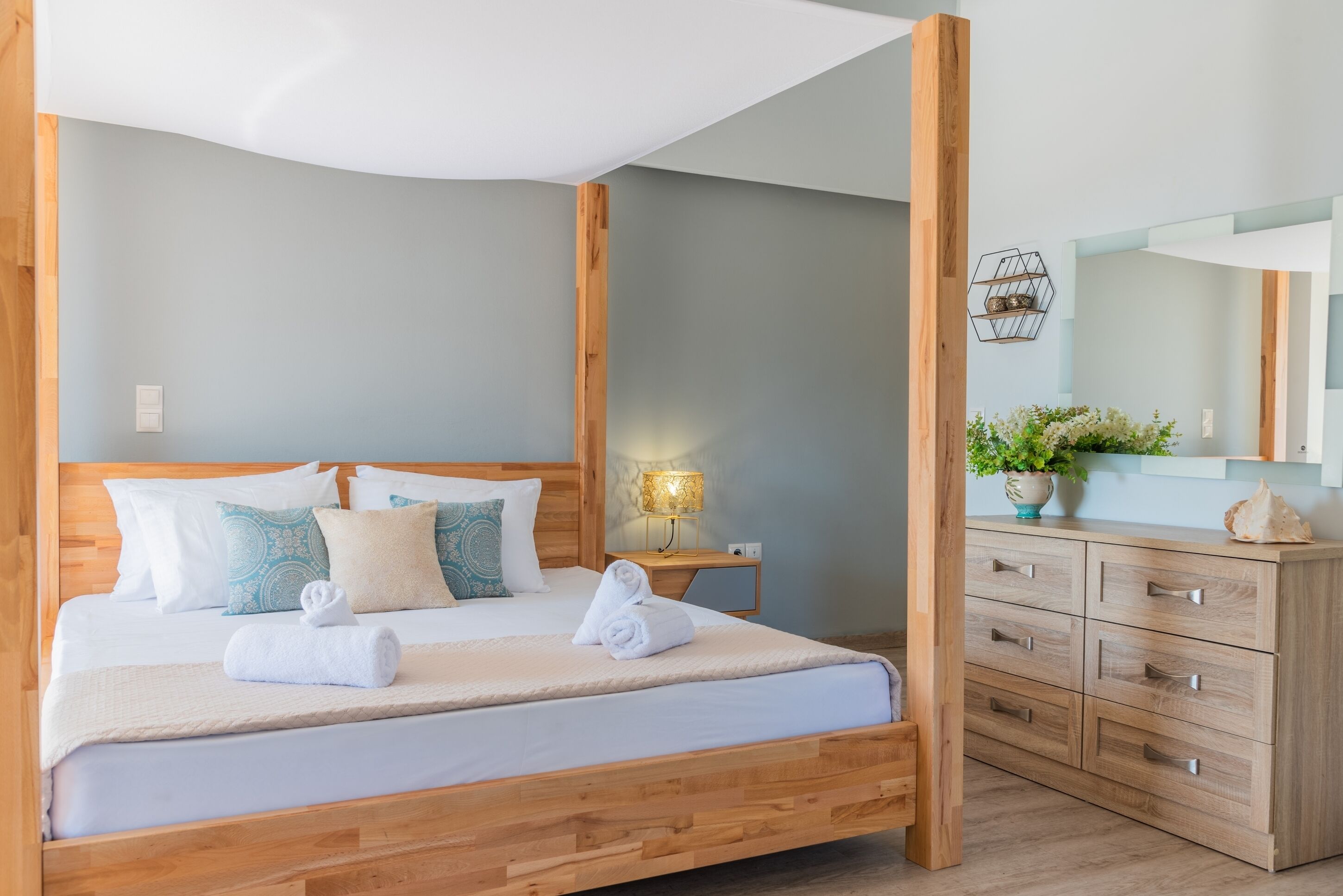 A neatly made bed with white linens and a wooden headboard, a wooden nightstand with a lamp, and a wooden dresser with drawers.