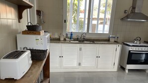 A kitchen with white cabinets, a toaster, a kettle, and a stove. - Casa na Praia do Canto - 6 Quartos - Búzios (Armação dos Búzios)