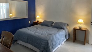 A bedroom with a bed, two bedside tables with lamps, a wooden chair, a mirror, and an air conditioning unit. - Casa na Praia do Canto - 6 Quartos - Búzios (Armação dos Búzios)