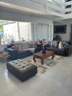 Un salon spacieux avec un canapé, un pouf et une table basse, un balcon avec vue et un téléviseur fixé au mur.