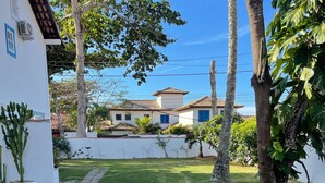 A well-maintained lawn with a stone pathway leading to a white building with blue windows. - Casa na Praia do Canto - 6 Quartos - Búzios (Armação dos Búzios)