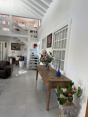 A spacious living area with a high ceiling, a wooden dining table, and a staircase leading to an upper level.