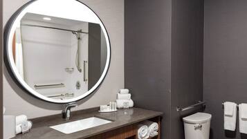 A modern bathroom with a round mirror, a sink, a toilet, and a towel rack.