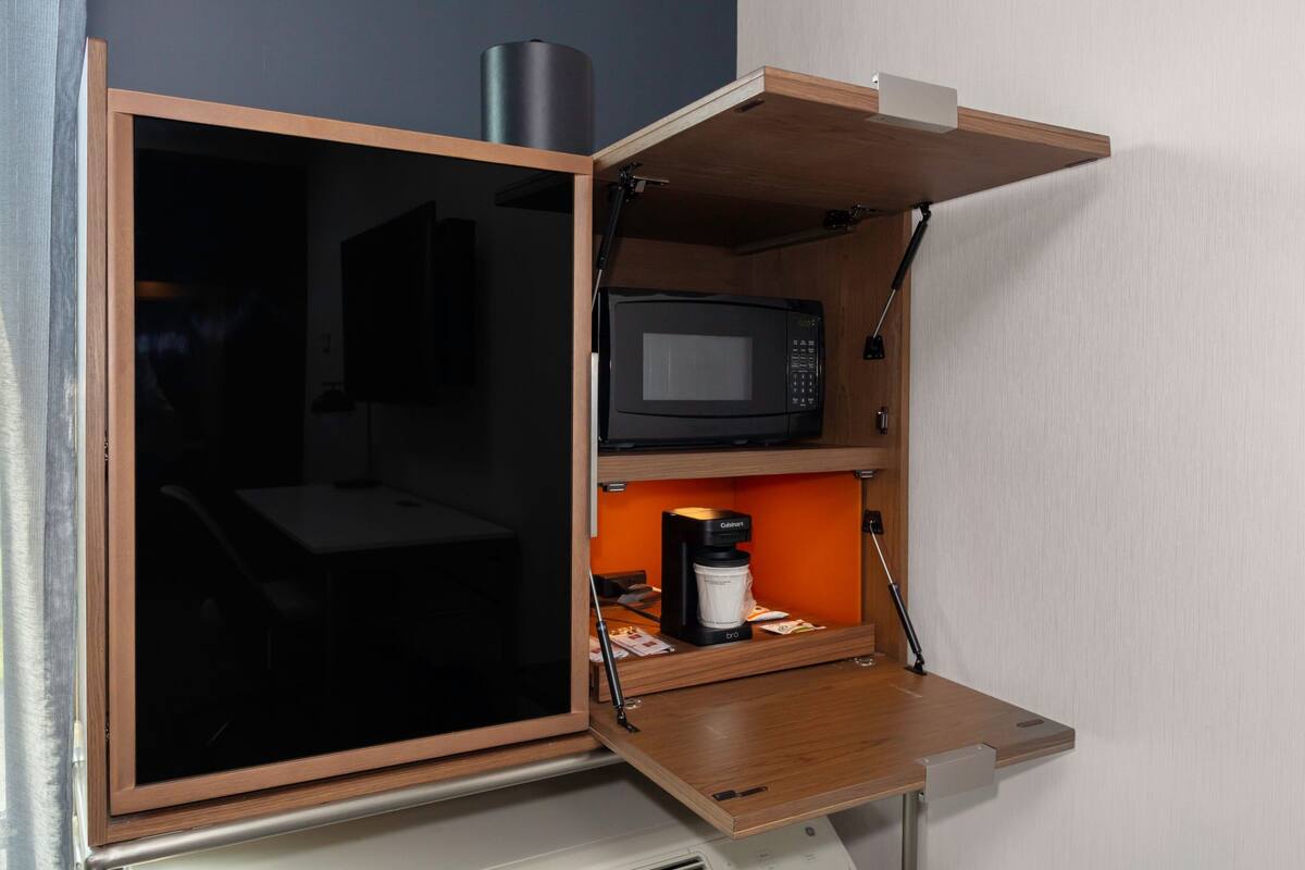 Een kleine keuken met een magnetron, koffiezetapparaat en een kastje.