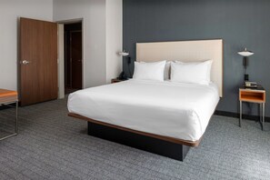 A hotel room with a large bed, two bedside tables with lamps, a wooden door, and a carpeted floor. - Courtyard by Marriott Memphis East/Galleria (Memphis)