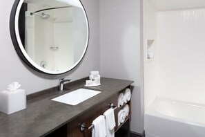 A bathroom with a round mirror, a sink, a towel rack, and a bathtub. - Courtyard by Marriott Memphis East/Galleria (Memphis)