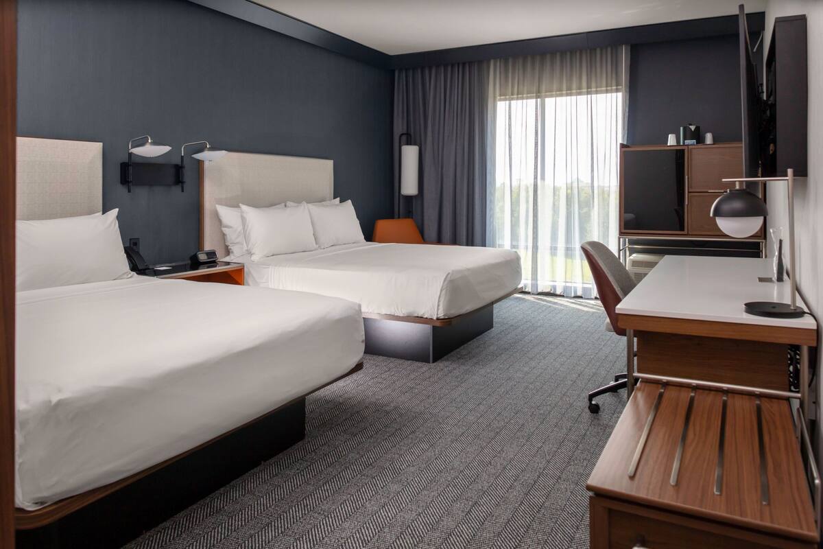 Een hotelkamer met twee bedden, een bureau, een stoel, een bureaulamp, een telefoon en een televisie.