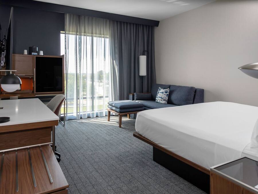 A modern hotel room with a large bed, a desk, a chair, and a sofa.
