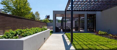 A modern outdoor patio area with a concrete pathway, wooden slatted wall, and a covered seating area.