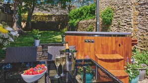 A patio with a wooden table, a bowl of fruit, and a wine cooler. - Coniston House (Cheltenham)