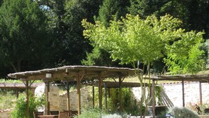 A rustic outdoor seating area with a stone wall, wooden pergola, and a gravel ground. - Chateau Du Mas - Classic, Elegant, Beautiful (Dignac)