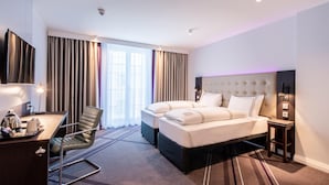 A hotel room with a bed, a desk, a chair, a TV, and a window with curtains. - Premier Inn Leipzig City Oper (Leipzig)