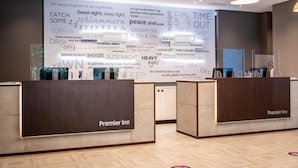 A hotel reception area with a large wall displaying various phrases and the hotel's name, 'Premier Inn.' - Premier Inn Leipzig City Oper (Leipzig)