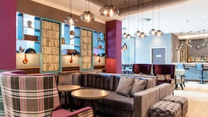 A modern lounge area with a sectional sofa, plaid chairs, a bar, and pendant lighting. - Premier Inn Leipzig City Oper (Leipzig)