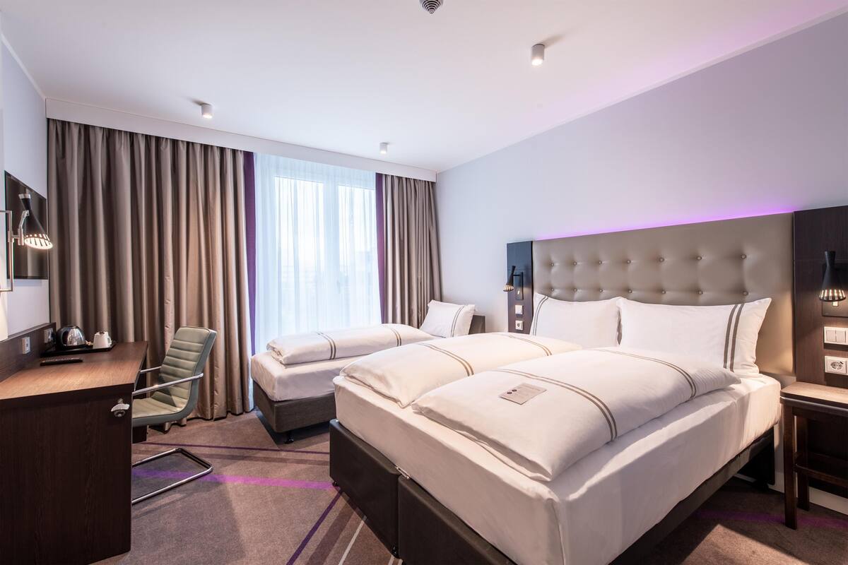 A hotel room with two beds, a desk, a chair, and a large window with curtains.