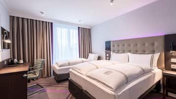 Ein Hotelzimmer mit zwei Betten, einem Schreibtisch, einem Stuhl und einem großen Fenster mit Vorhängen.