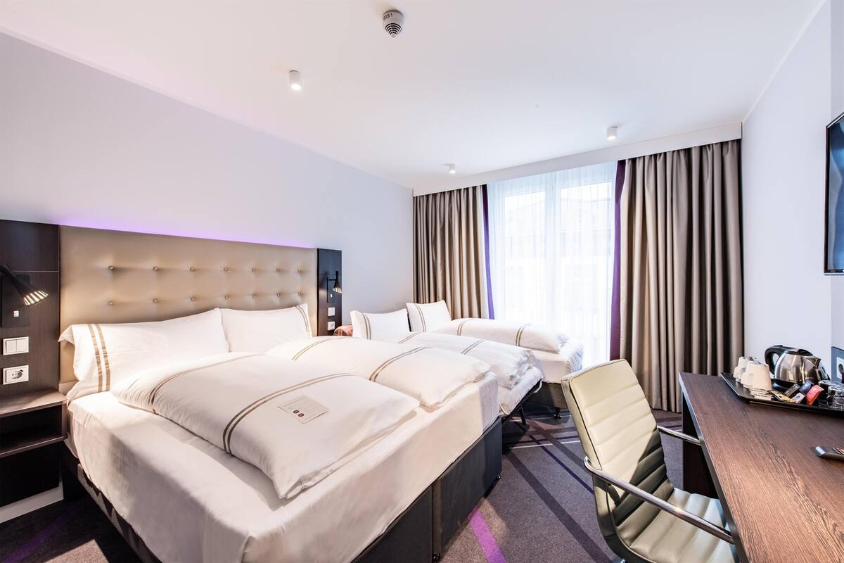 A hotel room with a large bed, a desk, a chair, a television, and a window with curtains.