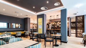 A modern restaurant with multiple dining areas, wooden tables, and chairs. - Premier Inn Leipzig City Oper (Leipzig)