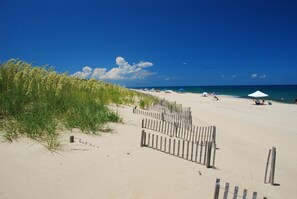 Een strand met een houten hek, strandparasols en een heldere blauwe lucht.