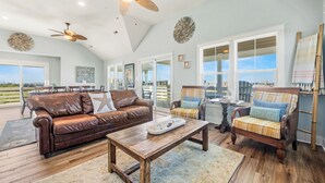 A spacious living area with a brown leather sofa, a wooden coffee table, and striped armchairs. A ceiling fan and decorative wall art are visible. - Mariner's Star Five Bedroom Home in Nags Head with Private Pool and Hot Tub (Nags Head)