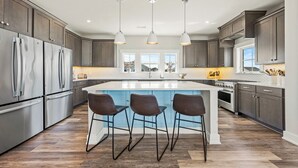 A modern kitchen with stainless steel appliances, a central island with bar stools, and pendant lighting. - Coastal Oasis in Corolla + Private Pool + Near the Beach (Corolla)
