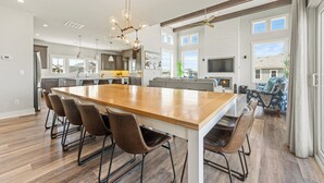 A modern kitchen with a large island, wooden flooring, and a dining area with six chairs. - Coastal Oasis in Corolla + Private Pool + Near the Beach (Corolla)