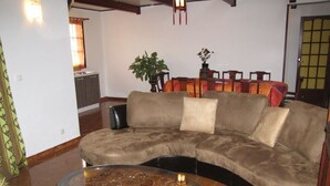 A living room with a curved sectional sofa, a glass-top coffee table, and a dining area with a table and chairs. - F3 apartment in the heart of Petite Ile (Saint-Pierre)