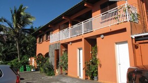 A two-story building with a balcony, potted plants, and a clear sky. - F3 apartment in the heart of Petite Ile (Saint-Pierre)