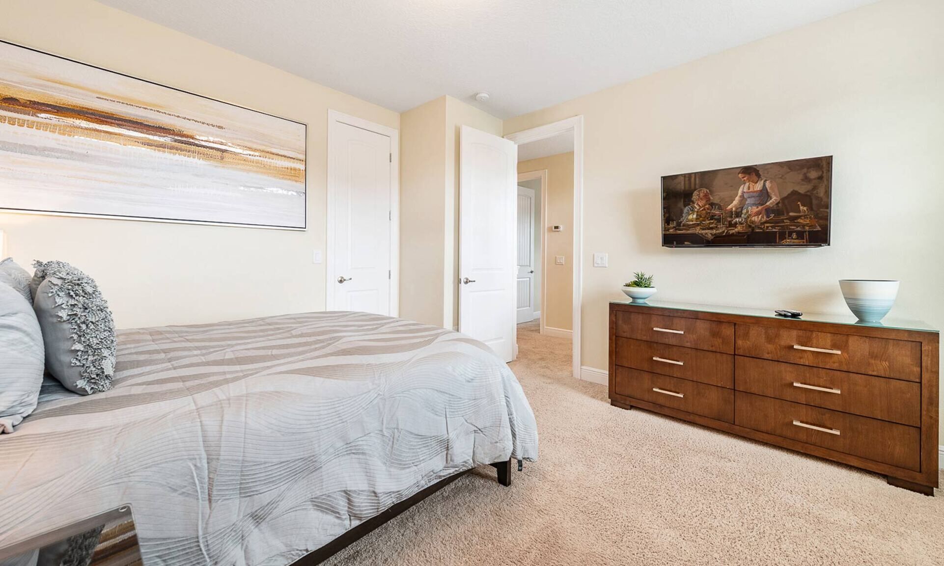 A bedroom with a bed, a dresser, a painting, and a door leading to another room.
