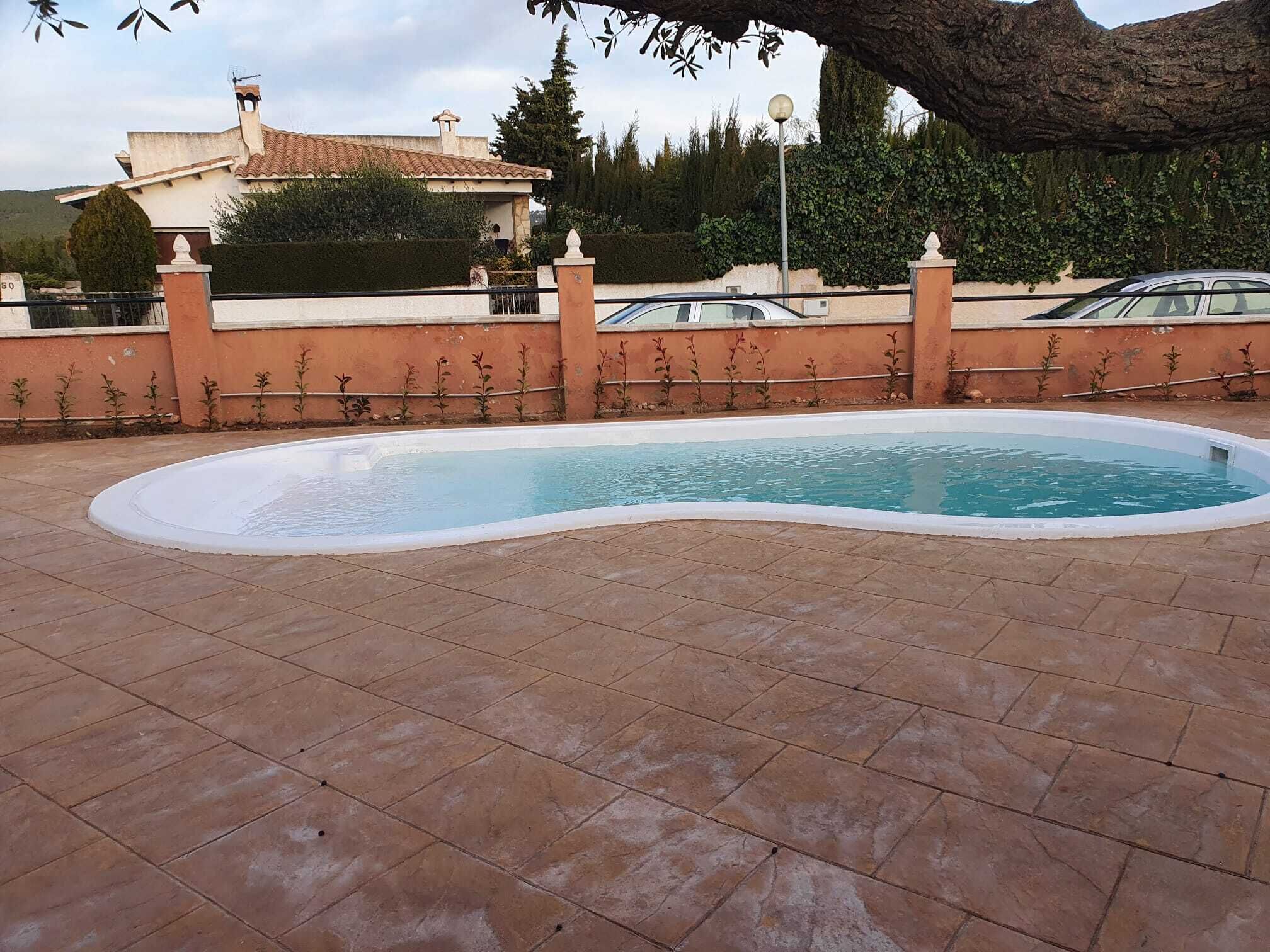 Una piscina con borde de baldosas, rodeada por un muro bajo y una valla.