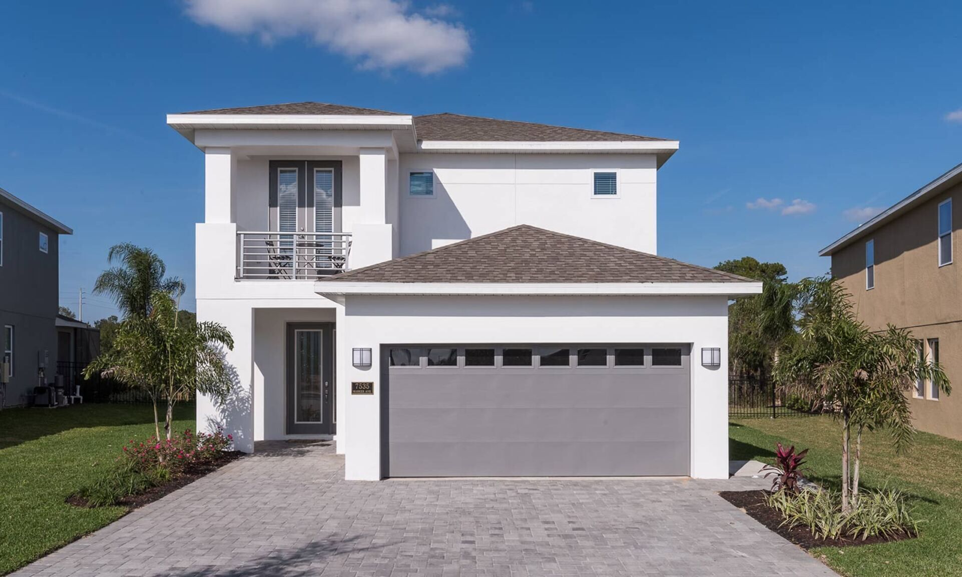 A two-story residential house with a garage, a balcony, and a well-maintained lawn.