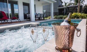 Une scène au bord de la piscine avec un jacuzzi, deux coupes à champagne et un seau à glace en cuivre contenant une bouteille de champagne.