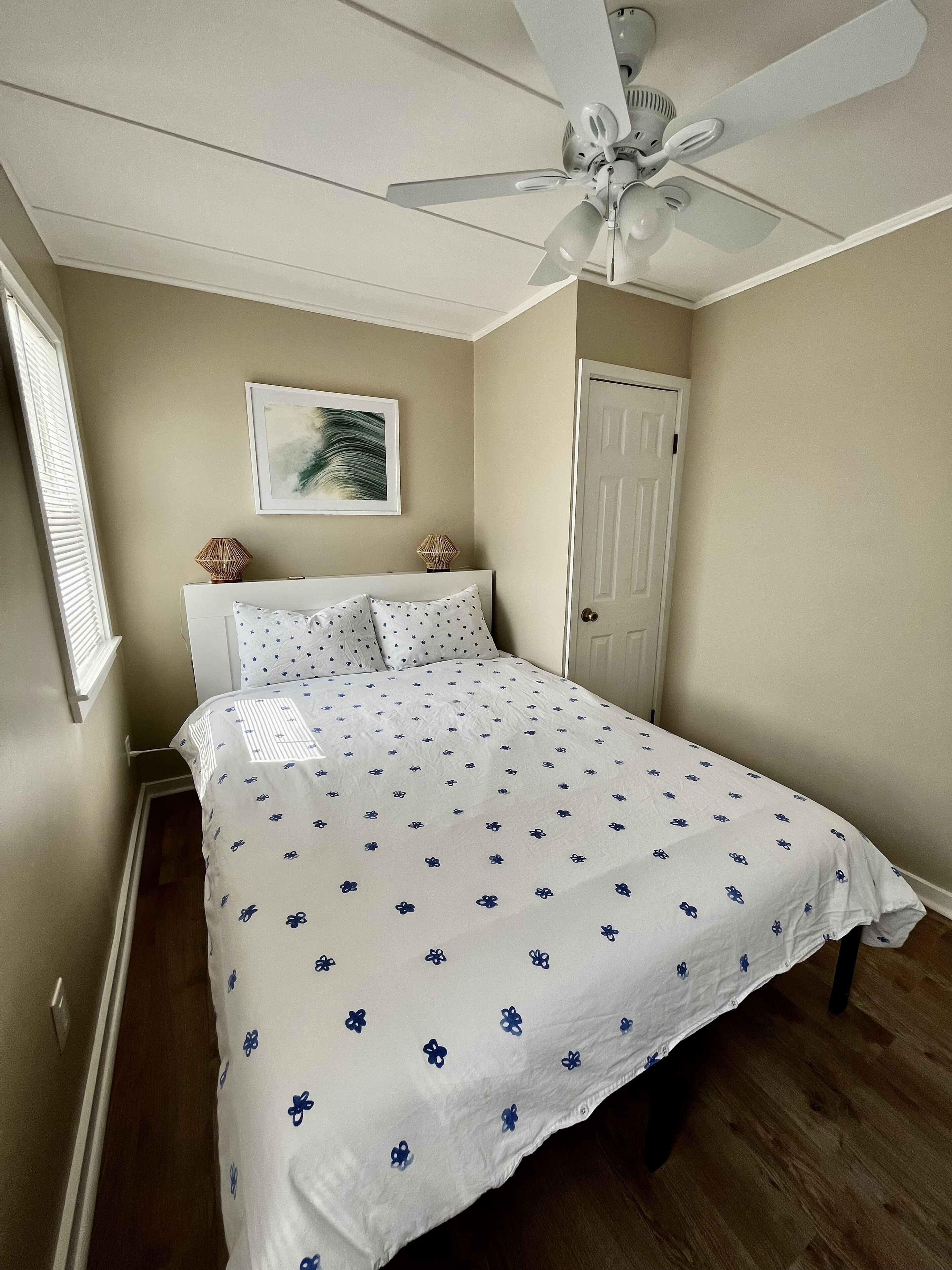 A bedroom with a bed, a ceiling fan, a door, and a window with blinds.