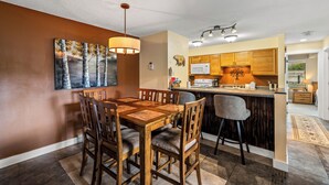 Un comedor con una mesa y sillas de madera, una cocina con armarios de madera y un cuadro en la pared.