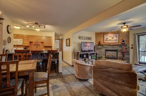 Cozy living room with a fireplace, TV, and dining area, featuring a comfortable sofa and wooden furniture.