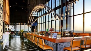 Zona de bar moderna con una barra larga, taburetes y vistas a la ciudad a través de amplios ventanales.