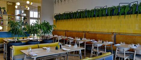 A restaurant interior with wooden tables and benches, hanging plants, and a patterned ceiling.